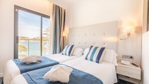 Et hotelværelse med to senge, et stort vindue med havudsigt, et sengebord med en lampe, og et natbord med telefon og fjernbetjening.