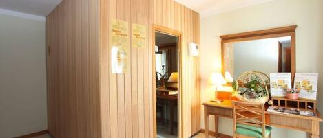 A sauna room with wooden walls, a desk, a chair, and informational posters.
