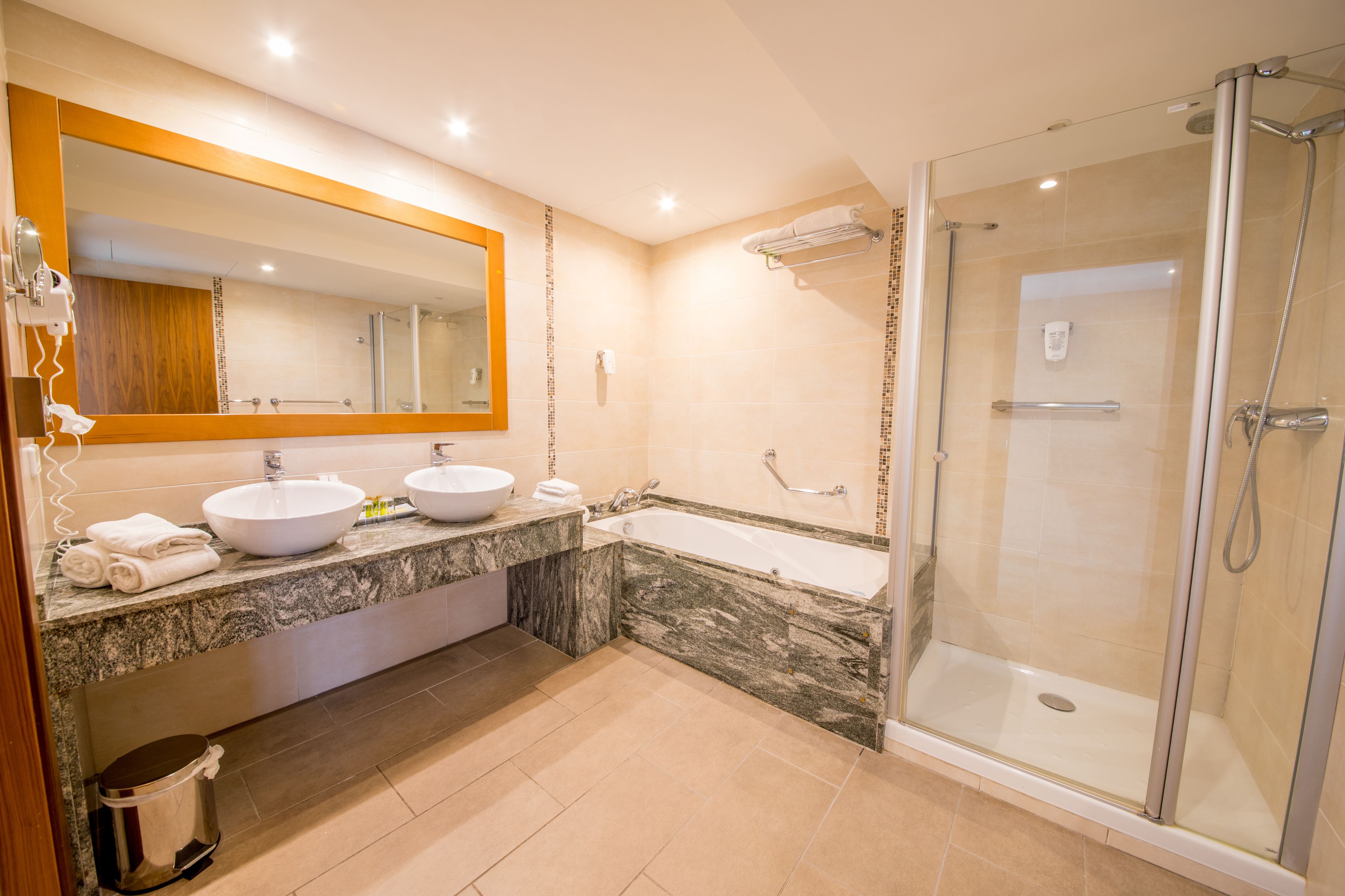 Een moderne badkamer met twee wastafels, een grote spiegel, een badkuip en een douche met glazen wanden.