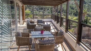 Un patio exterior techado con muebles de mimbre y una mesa, con vistas a un paisaje pintoresco.