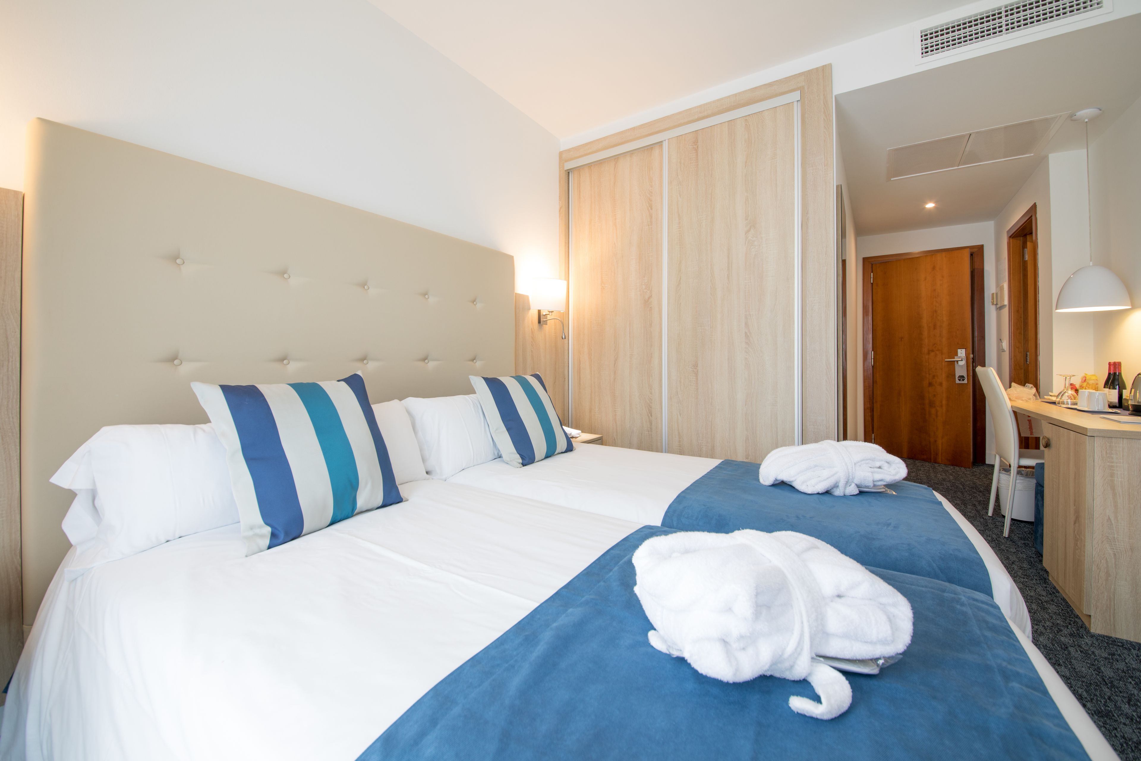 A hotel room with a large bed, two pillows, a blue bedspread, and two towels on the bed.
