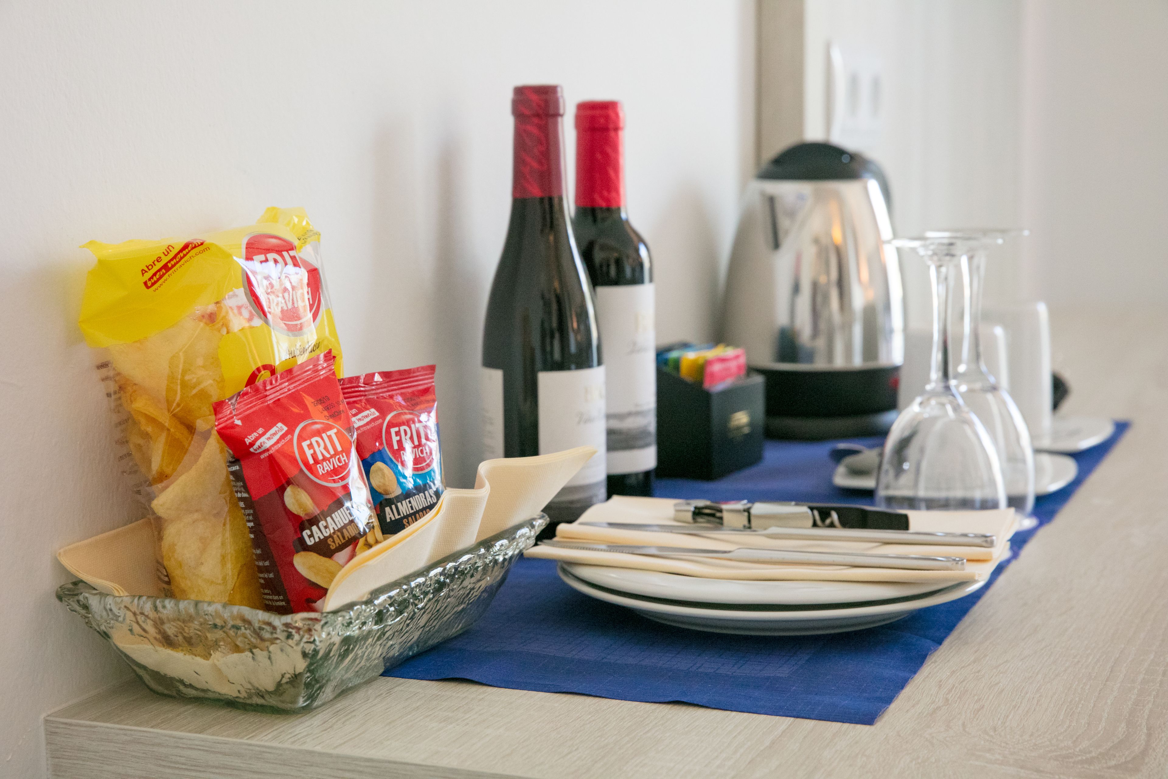 Un desayuno con un tazón de cereal, una bolsa de fruta, una botella de vino y una cafetera sobre una mesa.