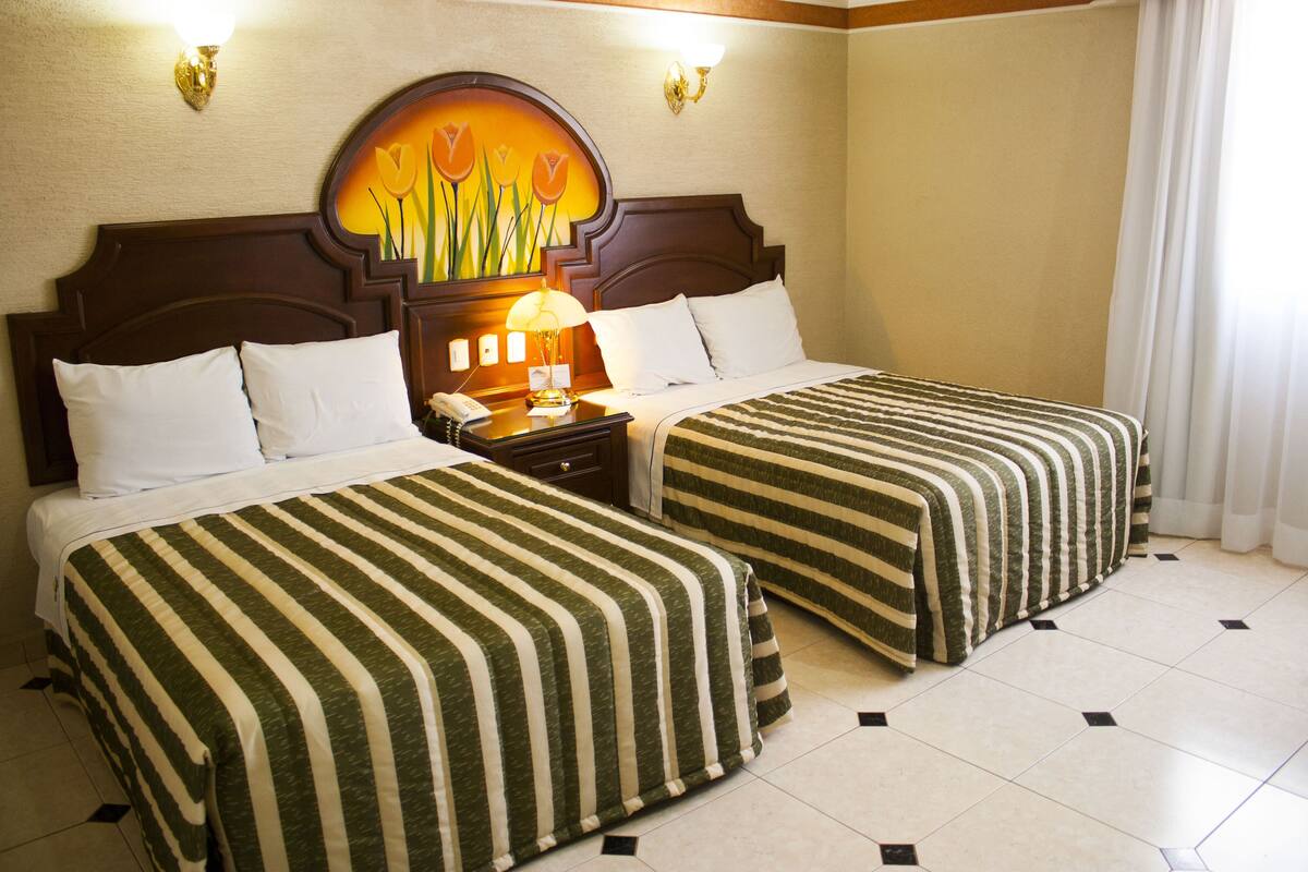 Una habitació d'hotel amb dos llits, una tauleta de nit, una làmpada i un quadre penjat a la paret.
