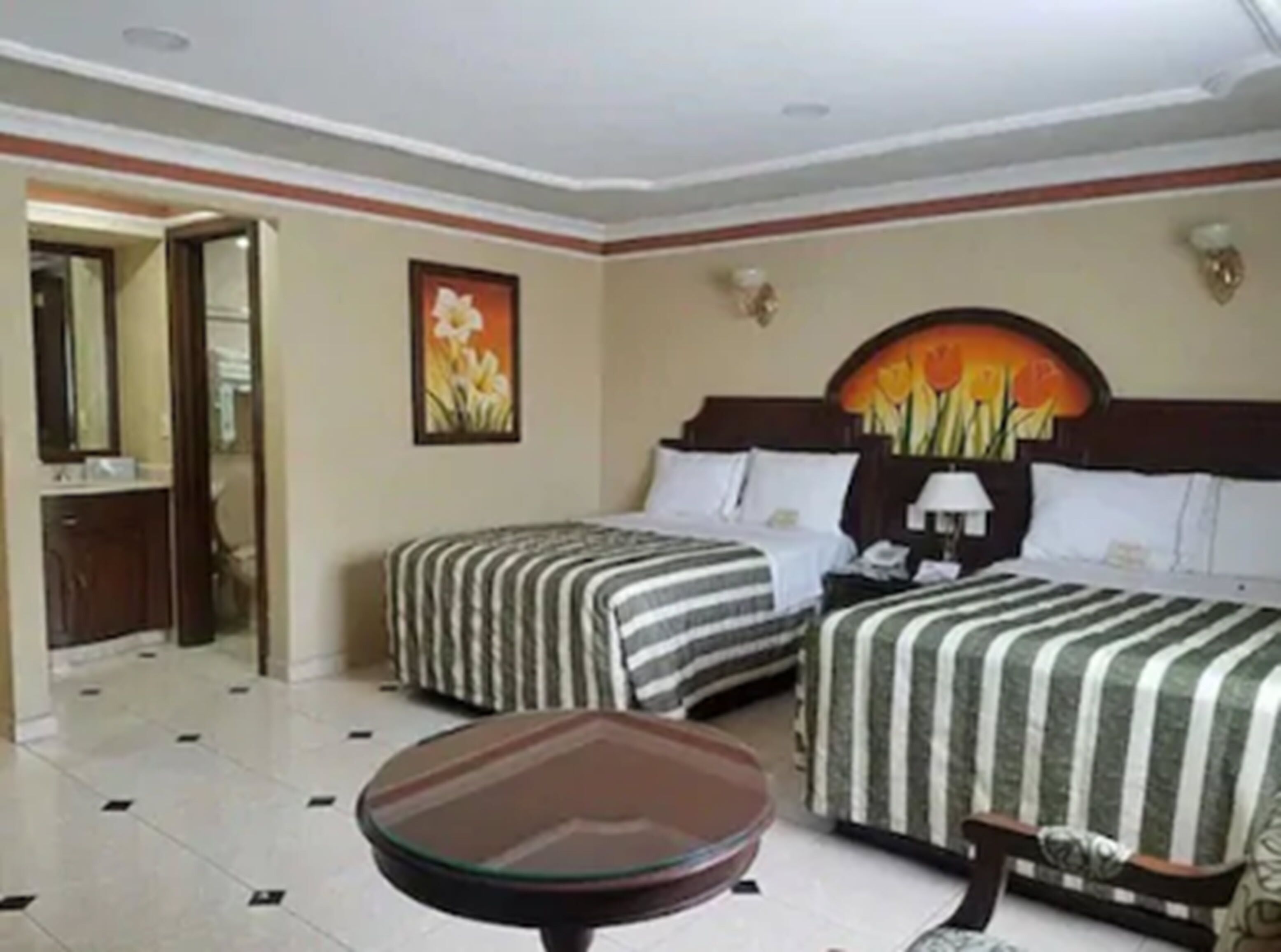 A hotel room with two beds, a small table, a nightstand, and a painting on the wall.
