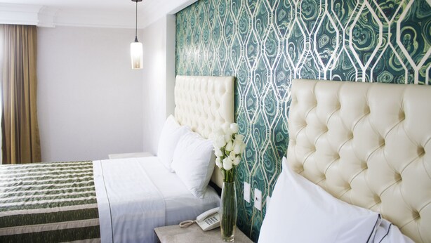 Una habitación de hotel con una cama, una mesita de noche con teléfono y un jarrón con flores.