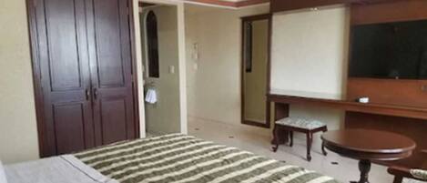 A hotel room with a bed, a wooden wardrobe, a television, and a small table.