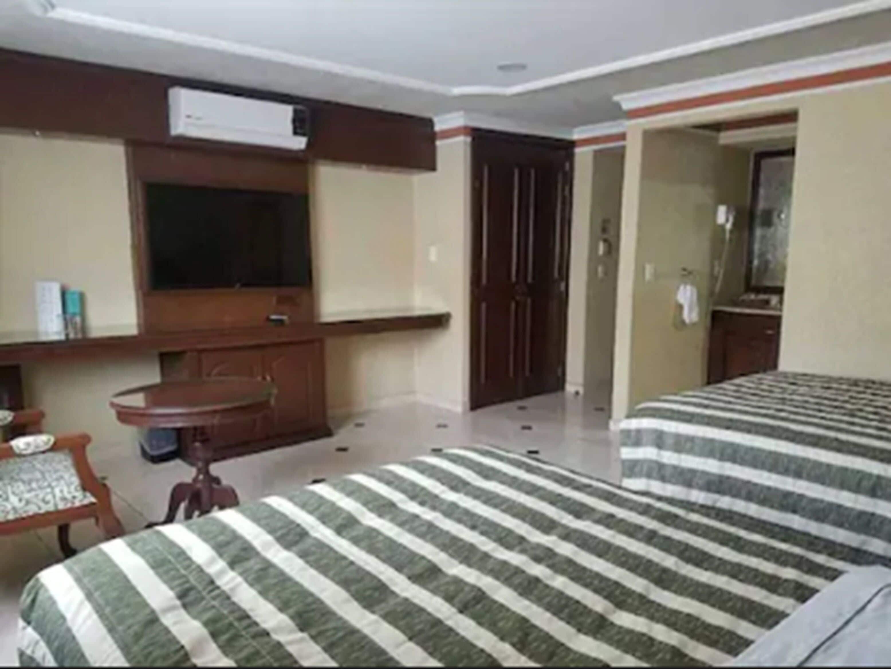 Camera d'albergo con due letti, una TV fissata al muro, una scrivania con una sedia e una porta che dà su un'altra stanza.