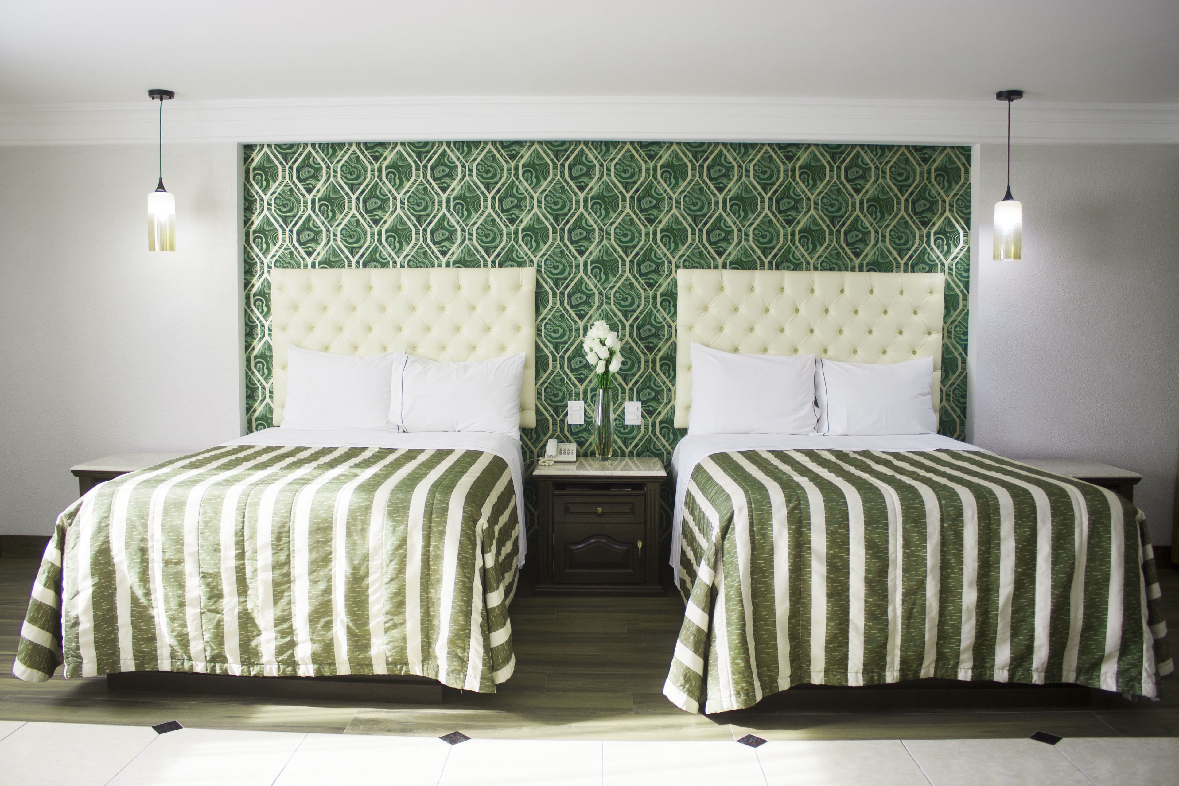 A twin room with two beds, a green patterned headboard, and bedside tables with lamps.