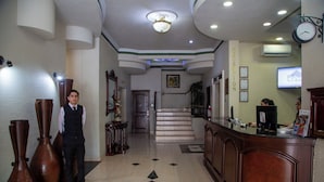 Un vestíbulo de hotel con mostrador de recepción, una escalera y un gran reloj en la pared.
