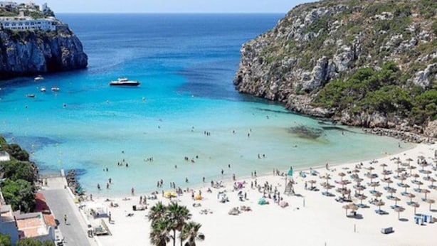 A beach with clear turquoise waters, a rocky coastline, and a large number of beach umbrellas and sun loungers. - Siesta Mar (Alayor)