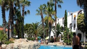 A swimming pool surrounded by palm trees and a building with a tiled roof. - Siesta Mar (Alayor)