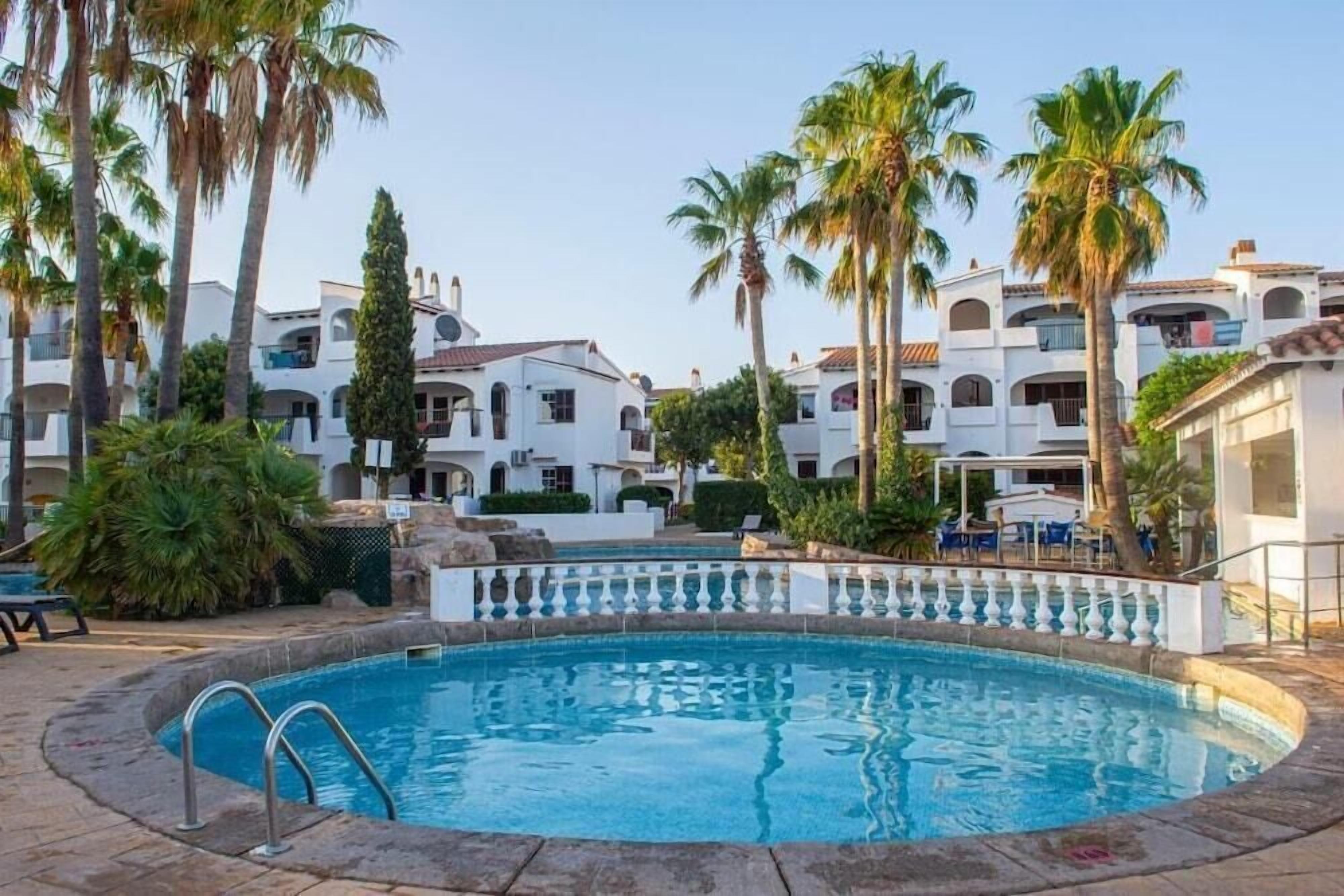 Ein Pool, umgeben von Palmen und weißen Gebäuden mit Balkonen.