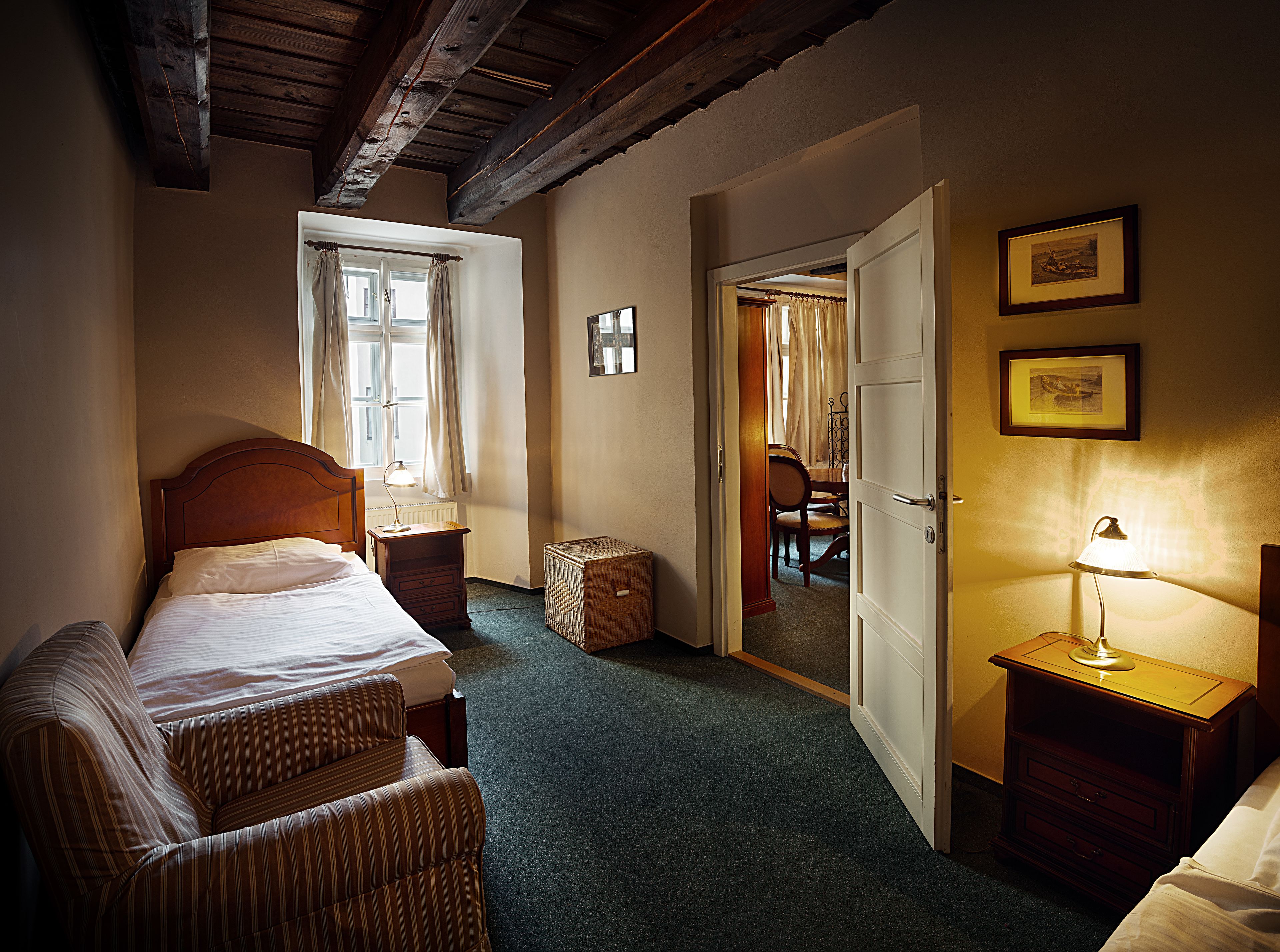 A hotel room with a bed, a chair, a nightstand, and a door leading to a dining area.