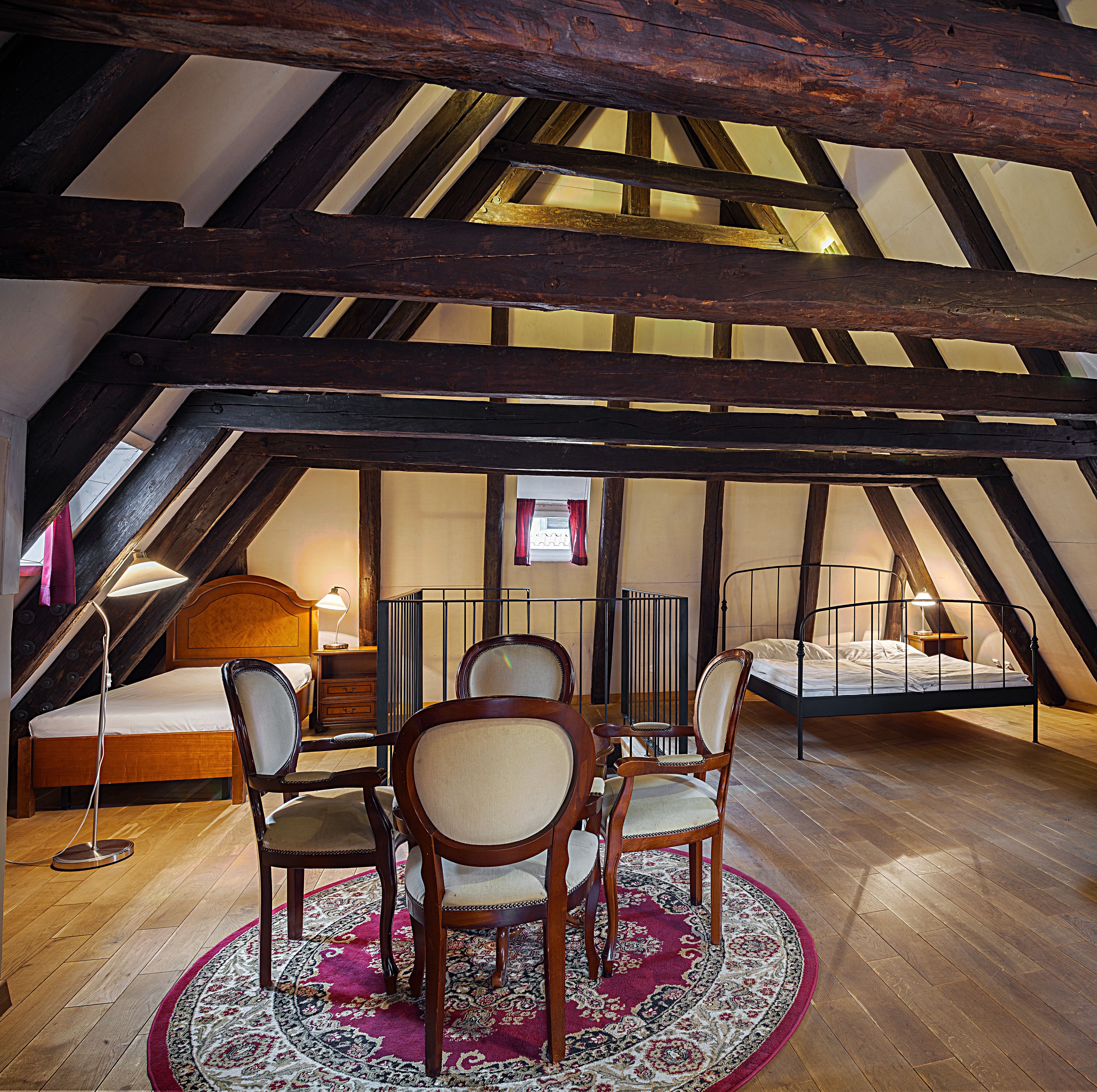 A cozy attic bedroom with a wooden ceiling, a bed, a desk, and a chair.