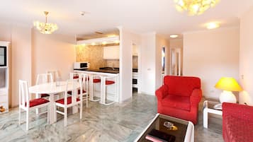 Un salon moderne avec un fauteuil rouge, un coin repas avec des chaises blanches et une cuisine en arrière-plan.