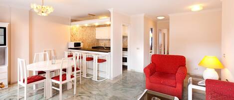 A modern living room with a red armchair, a dining area with white chairs, and a kitchen in the background.