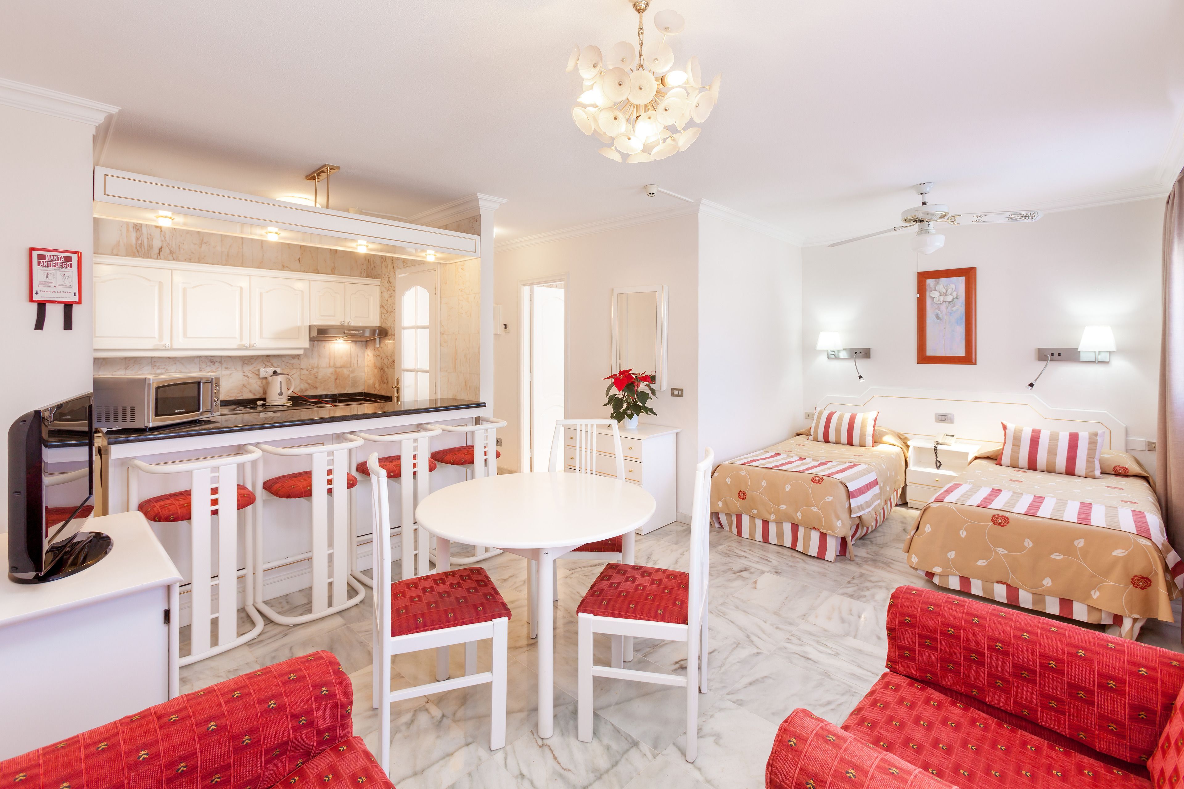 Une chambre d’hôtel avec un coin cuisine, une table à manger avec des chaises, un lit recouvert d’une couvre-lit à motifs et un canapé rouge recouvert de tissu.