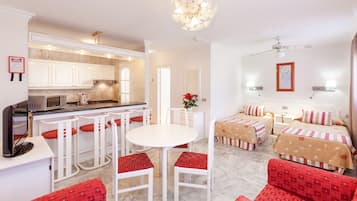 Habitación de hotel con cocina, una mesa de comedor con sillas, cama con colcha estampada y sofá tapizado rojo.