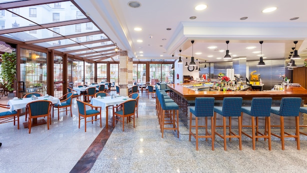 Un restaurante espacioso con techos altos, ventanas amplias y diversas opciones de asientos, incluyendo mesas y taburetes de bar.