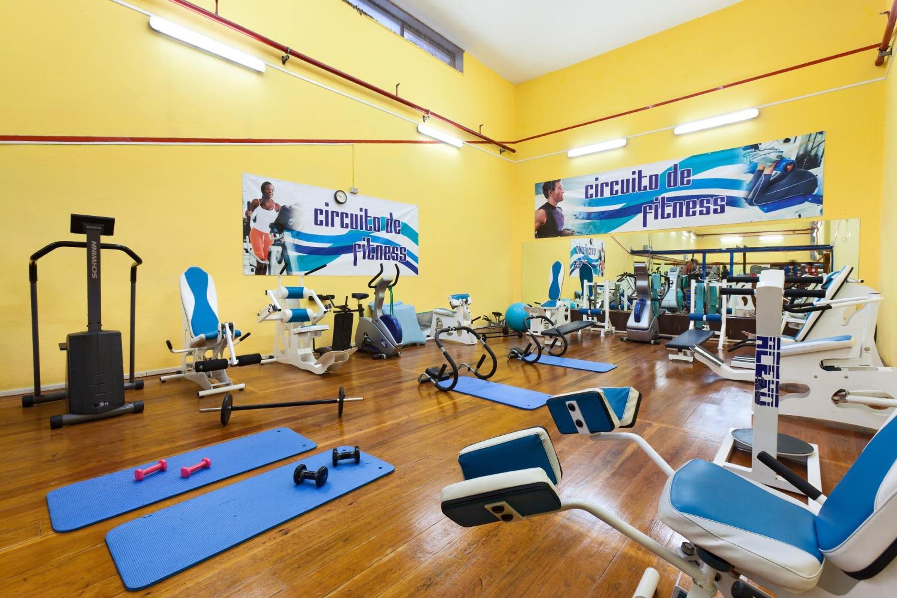 Un gimnasio con equipo de ejercicio, colchonetas de yoga y un espejo grande.