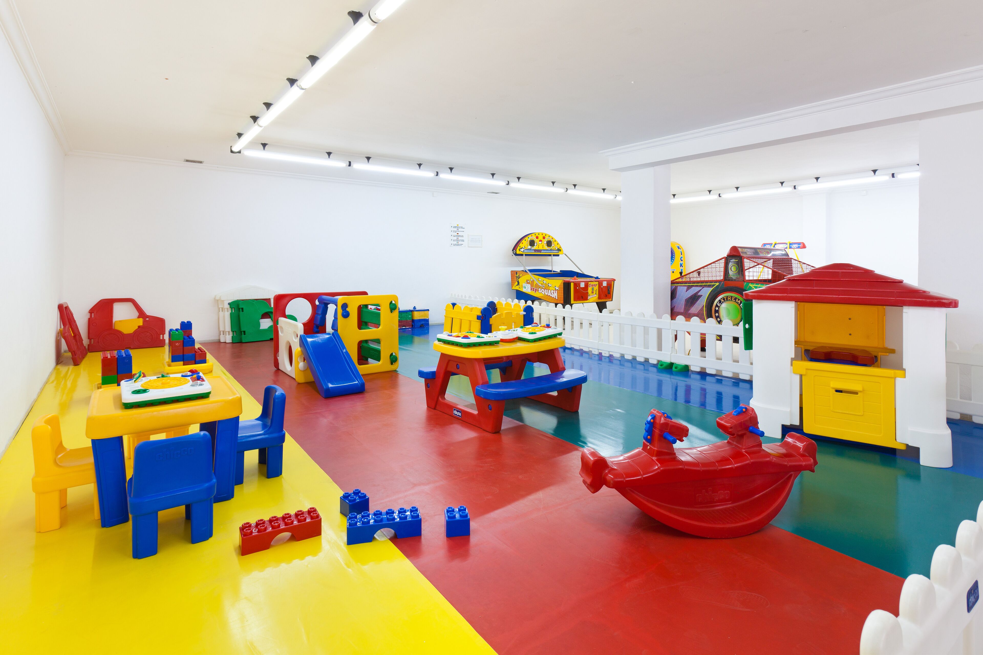 A brightly colored playroom with a yellow table, blue chairs, and various toys.