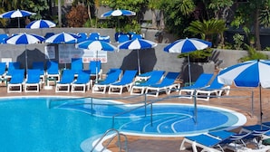 Un área de piscina con sombrillas azules y blancas, sillas de descanso y una piscina con diseño azul y blanco.