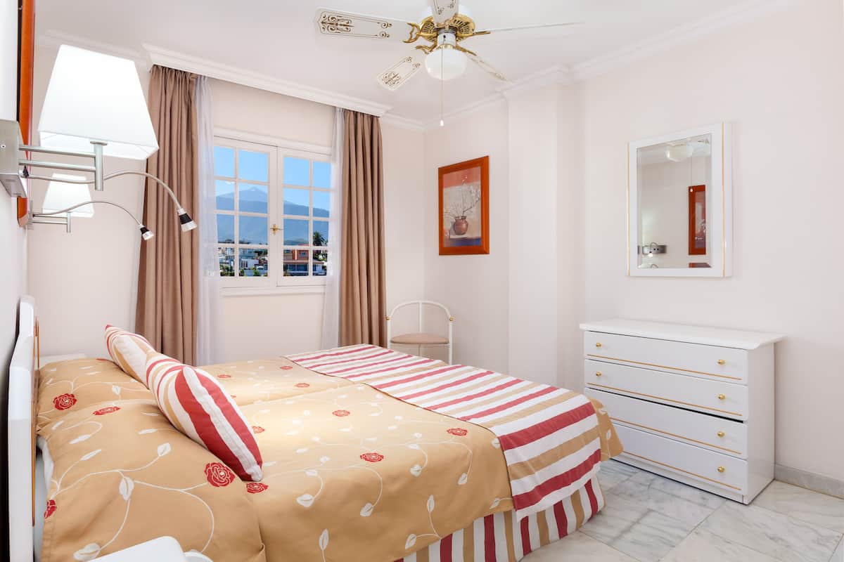 A bedroom with a bed, a dresser, a mirror, a window with curtains, and a ceiling fan.