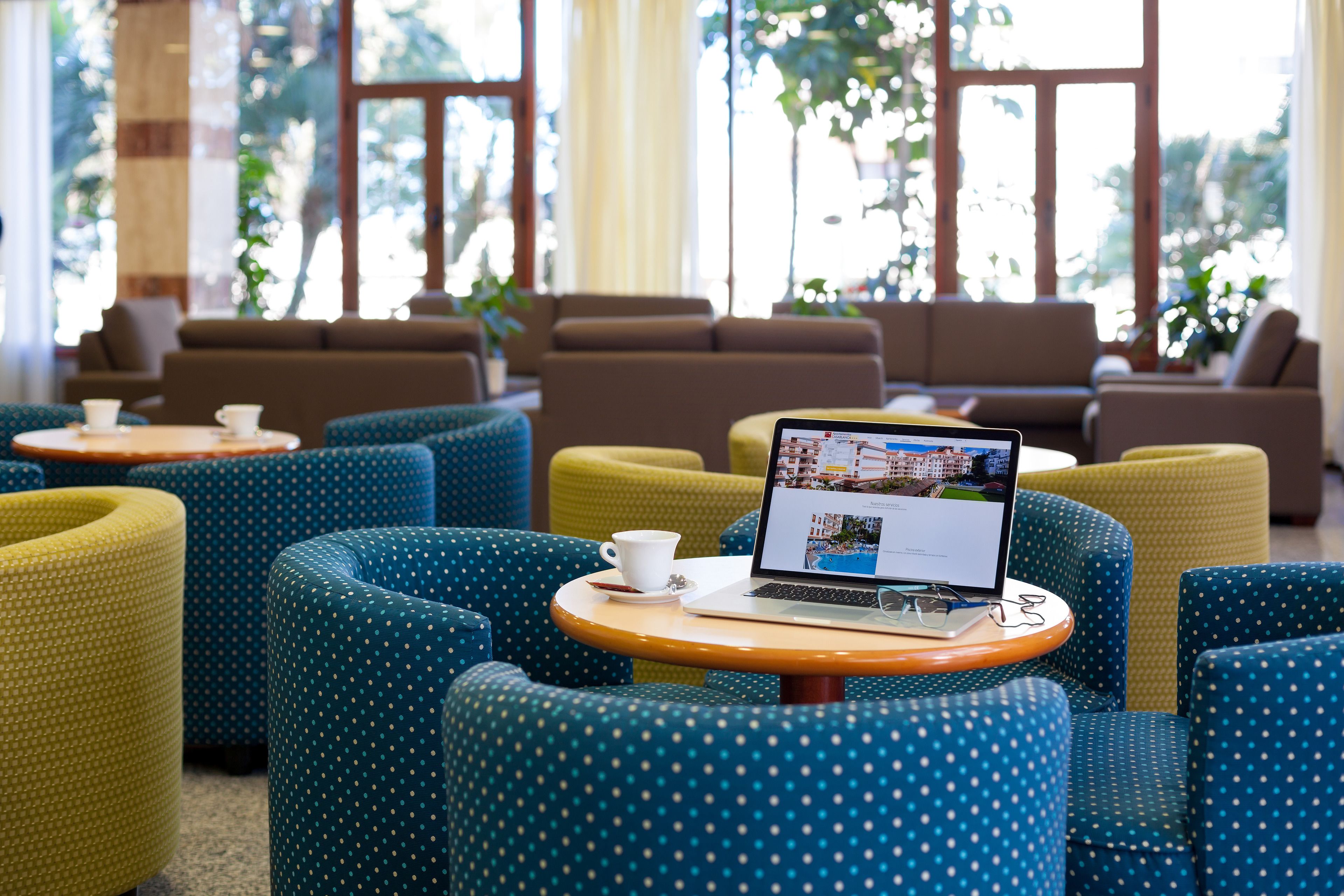 A seating area with blue and yellow chairs, a laptop on a small table, and a white cup.