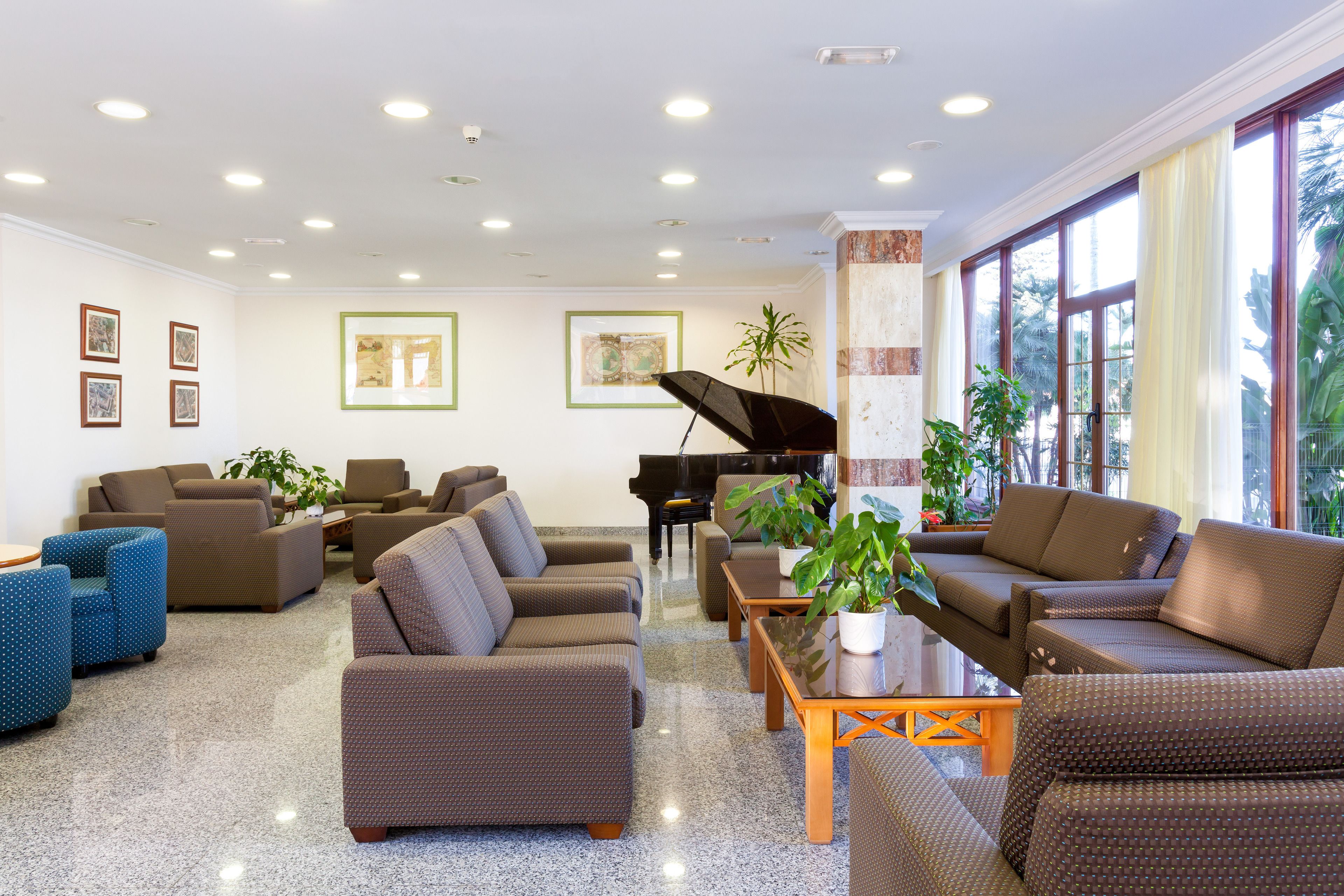 Eine geräumige Lobby mit verschiedenen Sitzbereichen, einem Flügel und großen Fenstern mit Blick ins Freie.