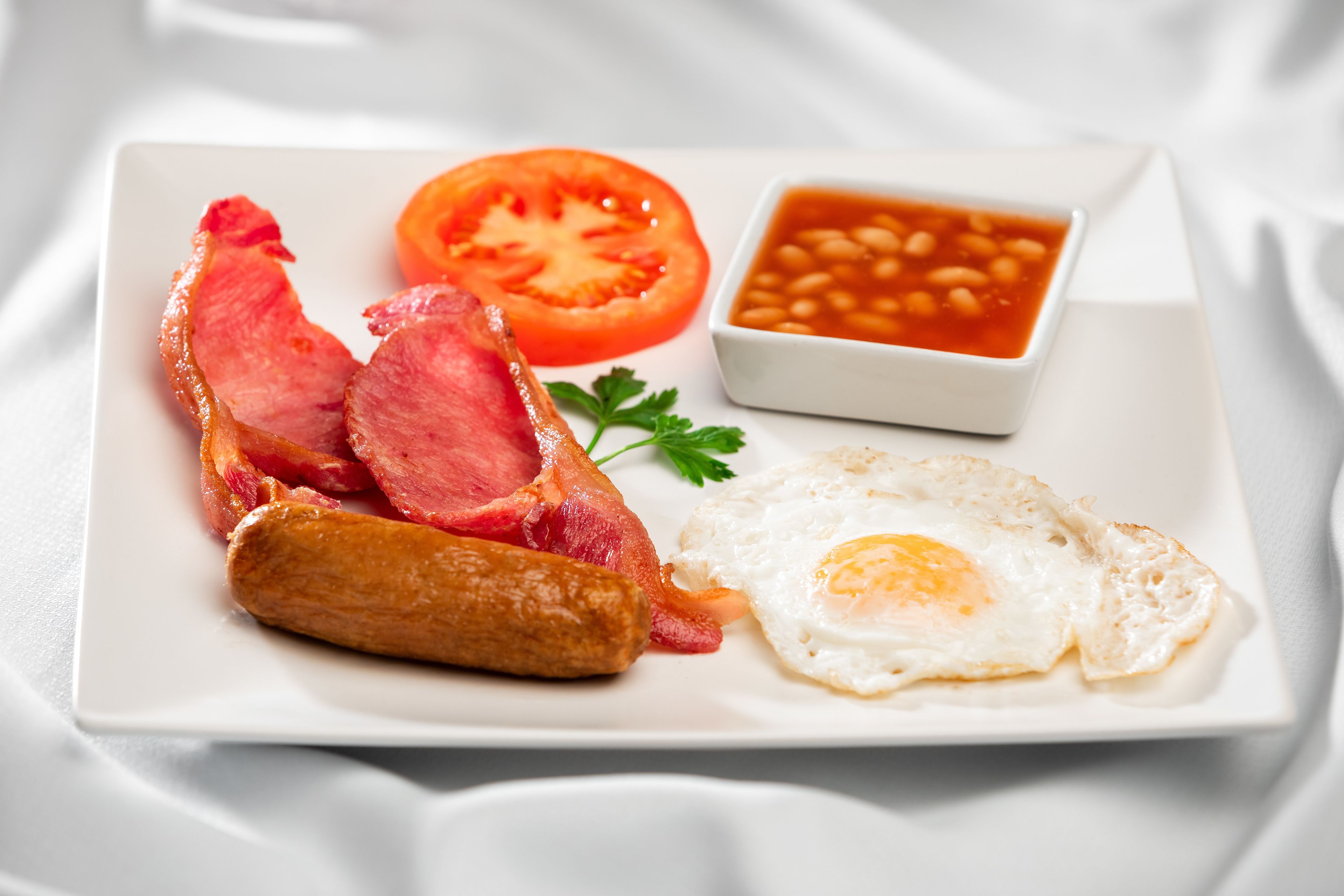 Un plato con tocino, un huevo frito, una rodaja de tomate y frijoles.