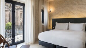 A hotel room with a large bed, a chair, a balcony with curtains, and a view of the city. - EME Catedral Mercer Hotel (Seville)
