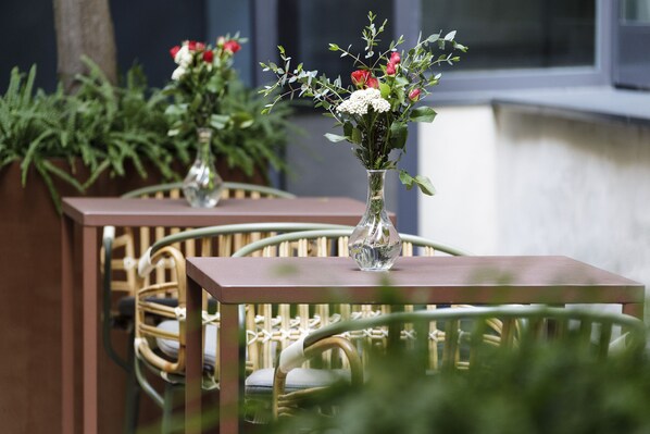 Two tables with vases of flowers, wicker chairs, and a wooden table.