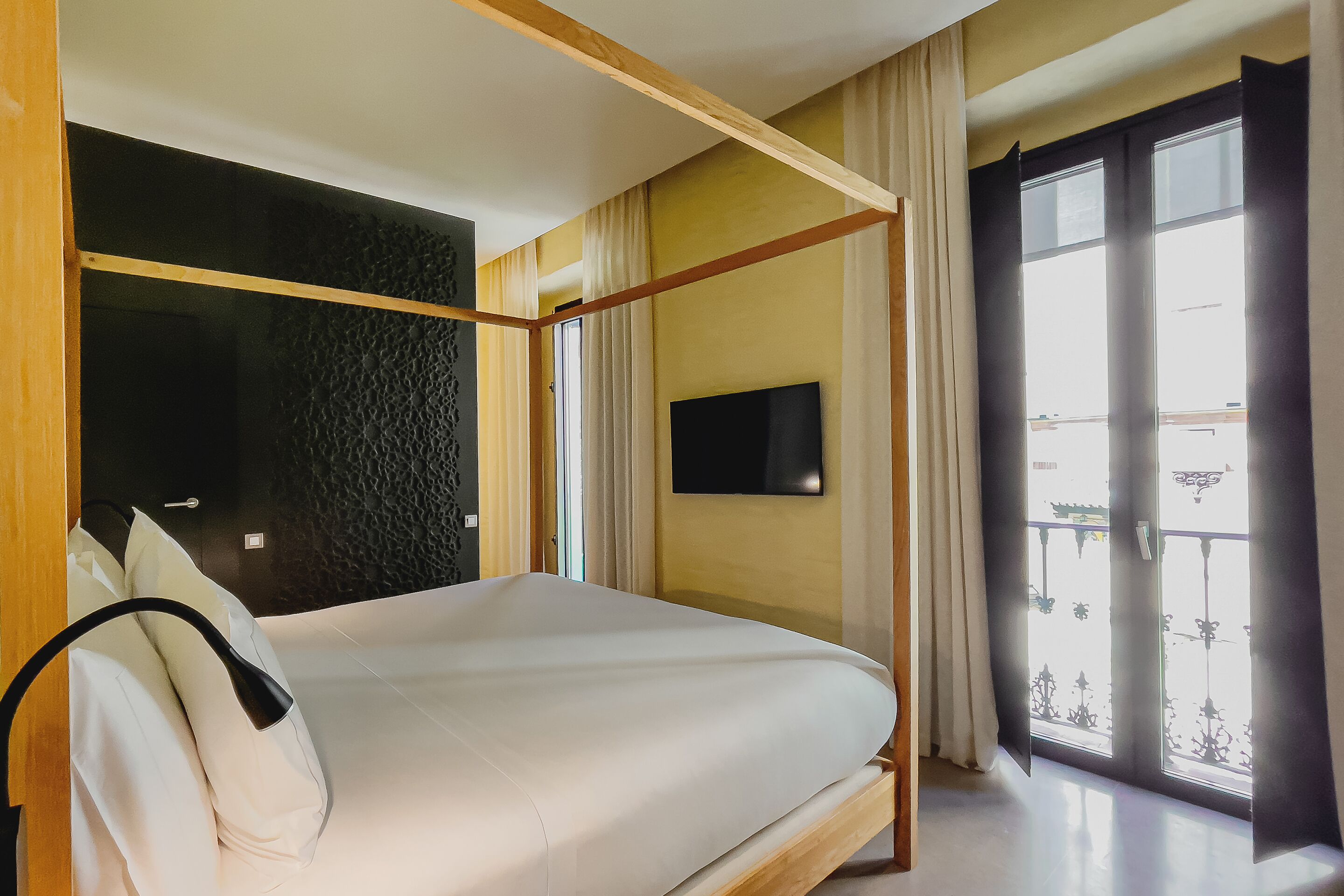 A bedroom with a bed, a TV mounted on the wall, and a window with a view of the outside.