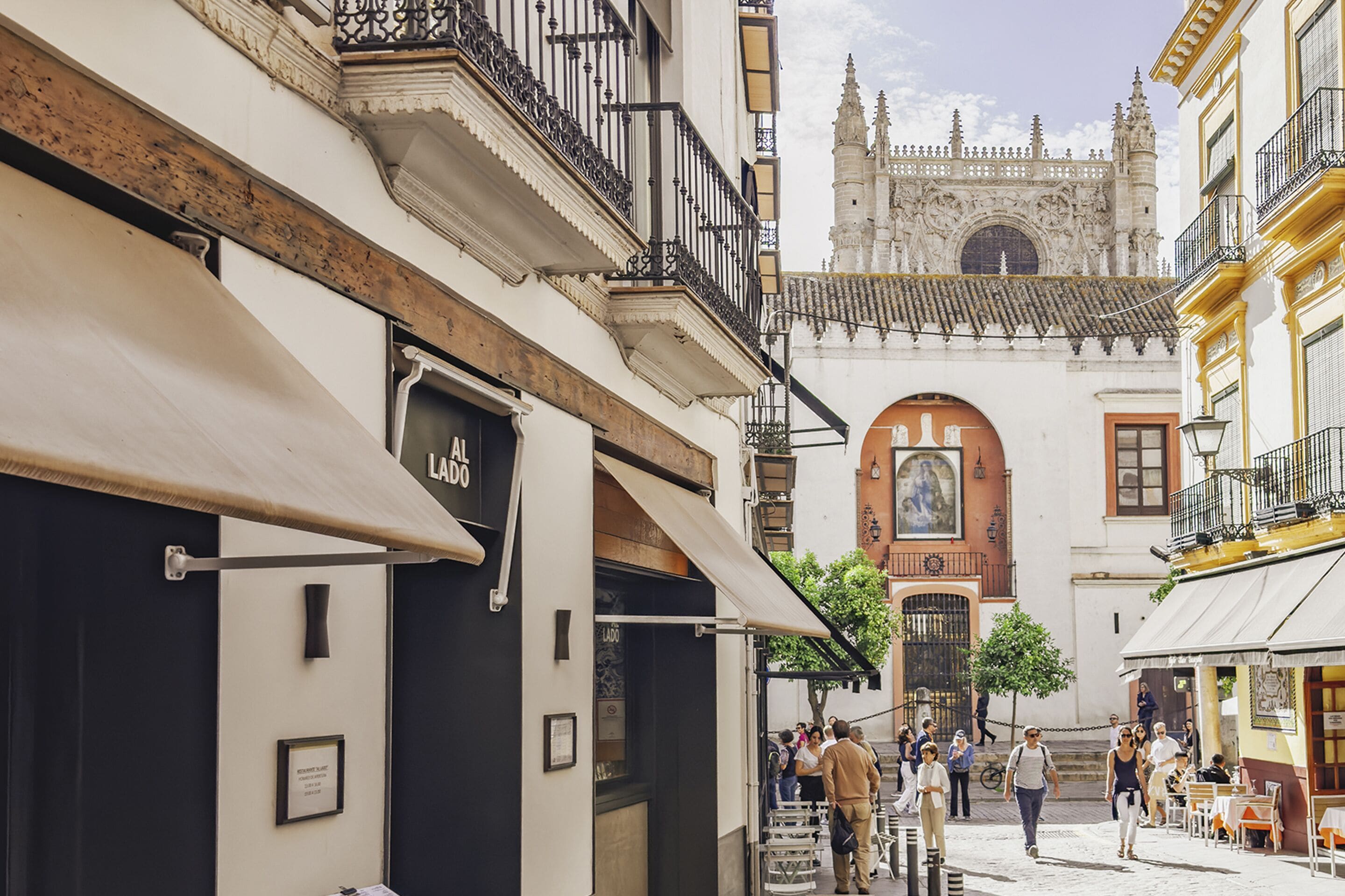 Una calle estrecha flanqueada por edificios, con una iglesia destacada y un gran arco, y gente caminando.
