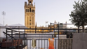 A balcony with two glasses of drinks, a tree, and a view of a historic tower. - EME Catedral Mercer Hotel (Seville)