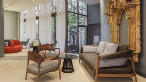 A modern living room with a sofa, chairs, a glass coffee table, and a decorative wall with intricate designs. - EME Catedral Mercer Hotel (Seville)
