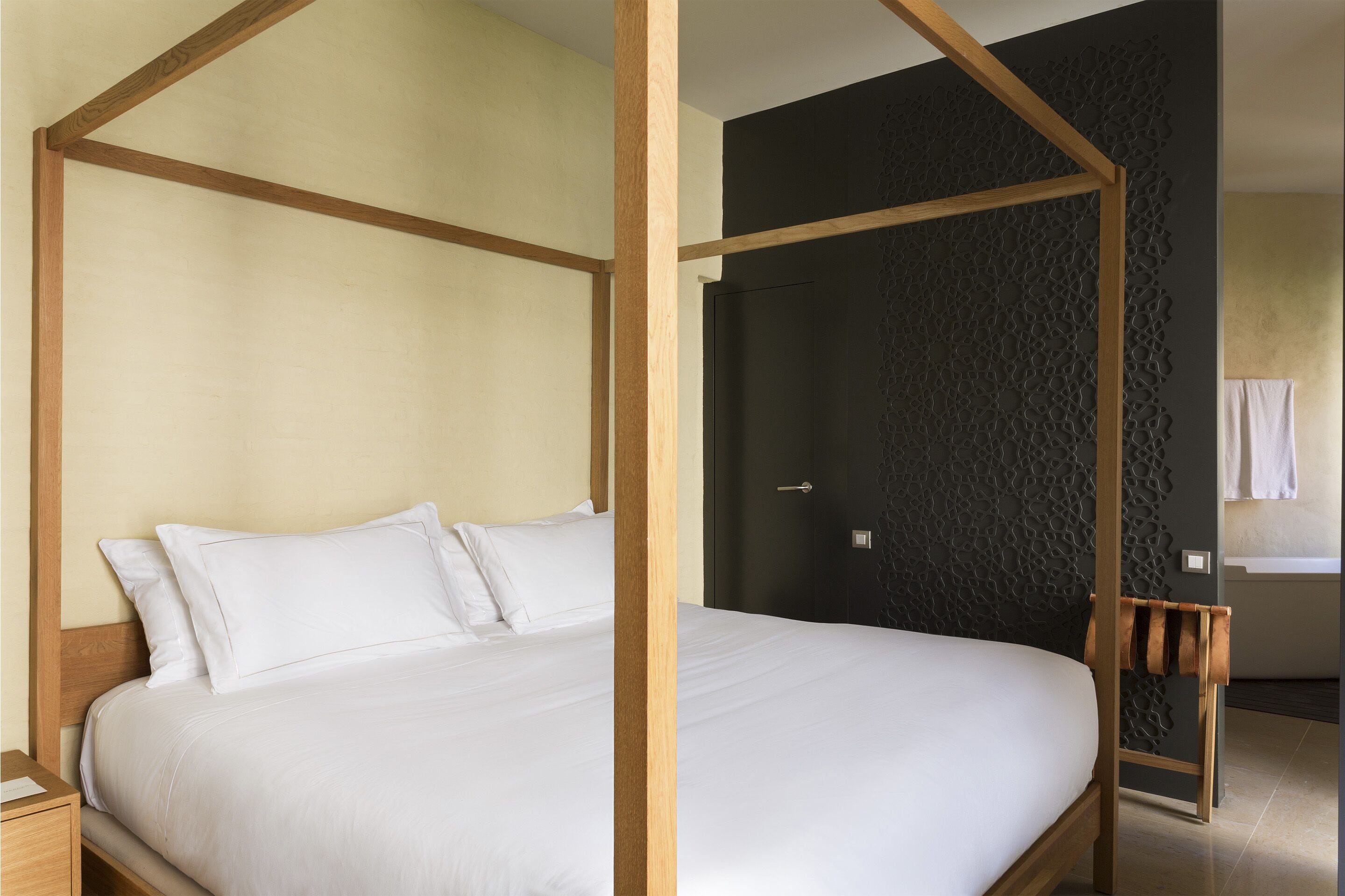 Un dormitorio moderno con una cama con dosel, una pared oscura con textura y una mesita de noche de madera.