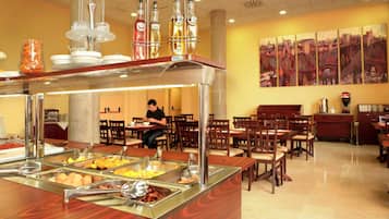 Een buffetgedeelte met verschillende food stations, een zithoek met tafels en stoelen, en een groot abstract schilderij aan de muur.