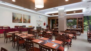 A dining area with multiple tables and chairs, a buffet setup, and a large painting on the wall.