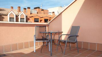 Un pequeño patio al aire libre con una mesa redonda y dos sillas, suelo de baldosas y vistas a edificios cercanos.