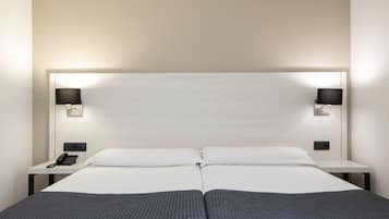 Habitación de hotel con dos camas, teléfono en la mesita de noche y lámparas de pared.