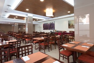 Ein großzügiger Hotel-Speisesaal mit mehreren Tischen und Stühlen, einem großen Gemälde an der Wand und einer Leinwand, die den Namen des Hotels zeigt.