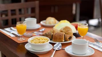 Una mesa de desayuno con cruasanes, cereales, jugo y una taza.