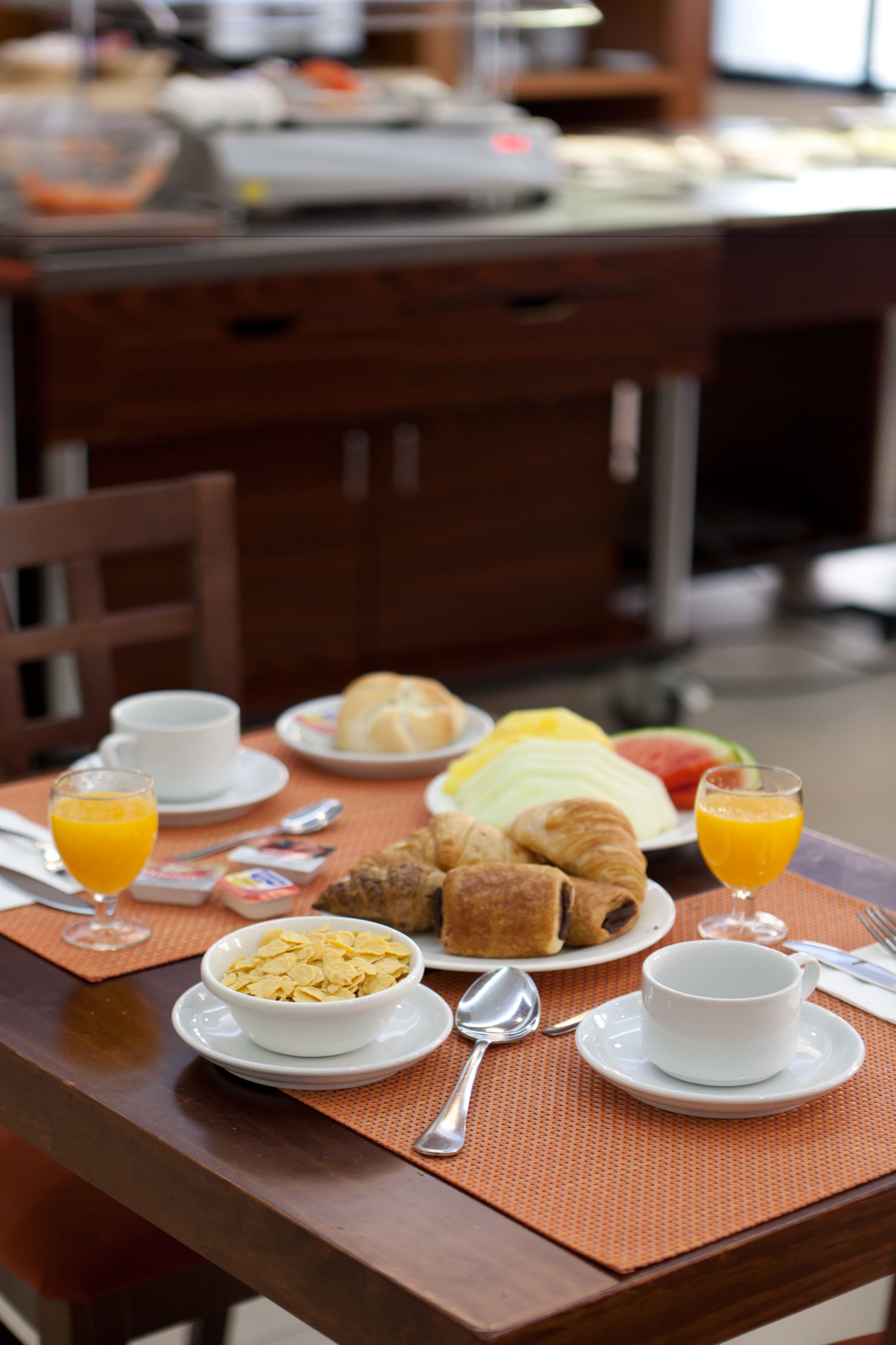 A breakfast table with plates of croissants, fruit, and cereal, along with glasses of orange juice.