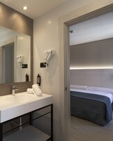Ein modernes Badezimmer mit einem weißen Waschbecken, einem Spiegel und zwei an der Wand befestigten Haartrocknern.