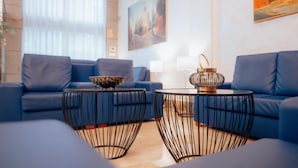 A modern living room with a blue sofa set, two black wireframe coffee tables, and a decorative lamp. - Hotel Porcel Ganivet (Madrid)