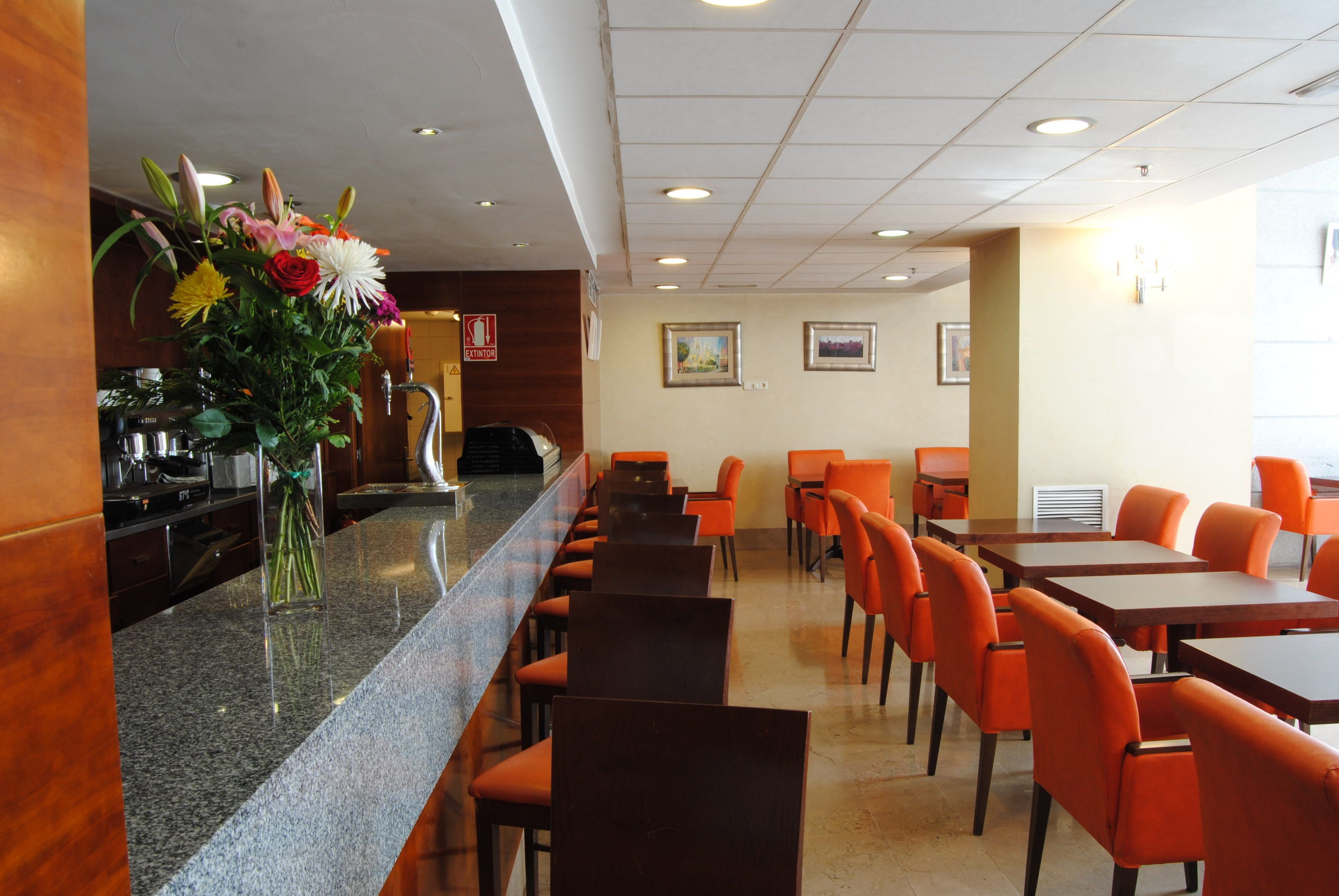 Un vestíbulo de hotel con una larga recepción, sillas naranjas y un arreglo floral.