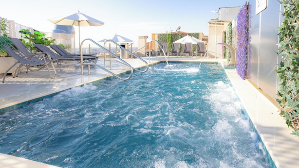 A pool area with lounge chairs, umbrellas, and a water feature. - Hotel Porcel Ganivet (Madrid)