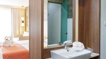 Habitación de hotel con tocador de madera, un espejo grande, una cama con colcha a cuadros rojos y blancos, y una mesita de noche con una bandeja de galletas.