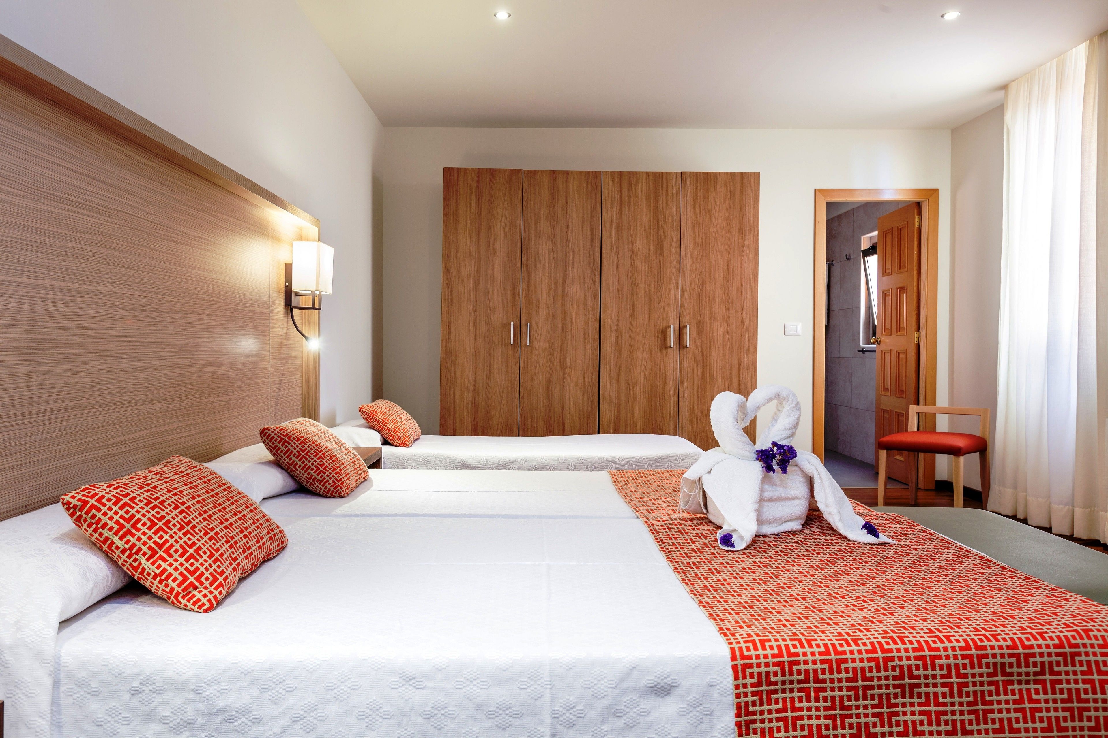 Ein Hotelzimmer mit zwei Betten, einem Holzschrank und einer Sitzecke mit einem Sessel.